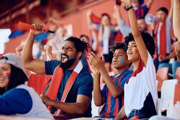 Happy black family cheering from stands during sports match at the stadium. - obrazy, fototapety, plakaty