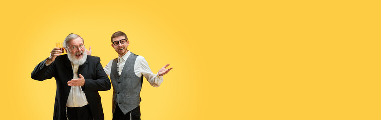 Banner. Two positive young and senior men posing in formal suits against yellow background with...