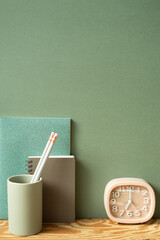 Stationery office supply. Notebook, pencil holder, clock on wooden desk. green wall background....