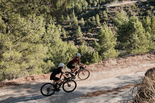 Two professional women cyclists riding gravel bicycles on a gravel road on a sunny summer day. Group bike ride in the natural countryside. Gravel advanture. Gravel cycling adventure. Alicante, Spain .