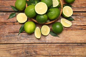 Fresh limes and green leaves with water drops on wooden table, flat lay. Space for text