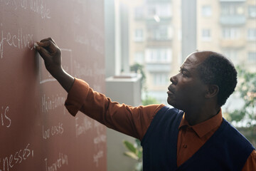 Side view portrait of Black college professor writing on chalkboard while preparing for lecture in...