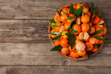 Fresh ripe juicy tangerines and green leaves on wooden table, top view. Space for text