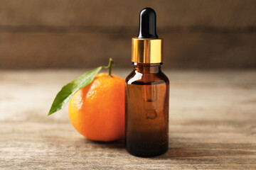 Bottle of tangerine essential oil and fresh fruit on wooden table, closeup