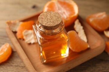 Bottle of tangerine essential oil and peeled fresh fruit on wooden table, closeup