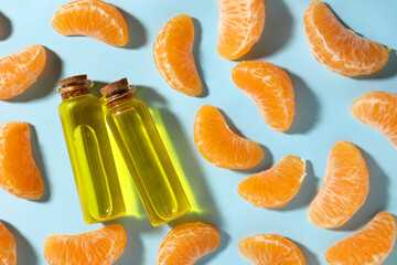 Aromatic tangerine essential oil in bottles and citrus fruits on light blue table, flat lay