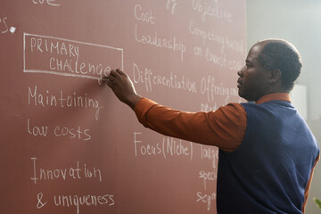 Side view portrait of African American college professor writing on chalkboard while preparing for...