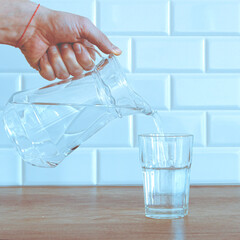 A glass of clean water on the kitchen table. A jug of water in a man's hand
