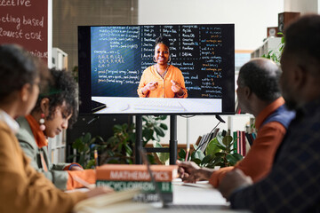 Black woman as professor on computer screen giving online class via remote technology to group of...