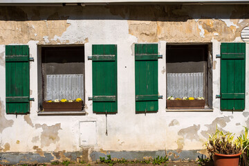 A house facade in need of renovation with two windows and green shutters
