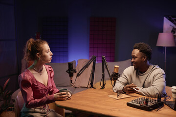 Smiling African American host at desk with studio equipment interviewing fashionable Caucasian...