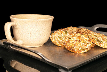 Several sweet thaler cookies with ceramic cup on metal tray, macro, isolated on black background.