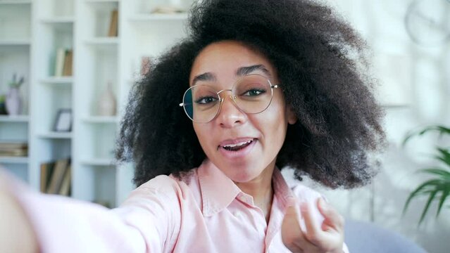 POV A young happy pretty african american female in glasses talking on a video call taking a selfie using a smartphone in home. A smiling black woman student has online chat with a friend or boyfriend