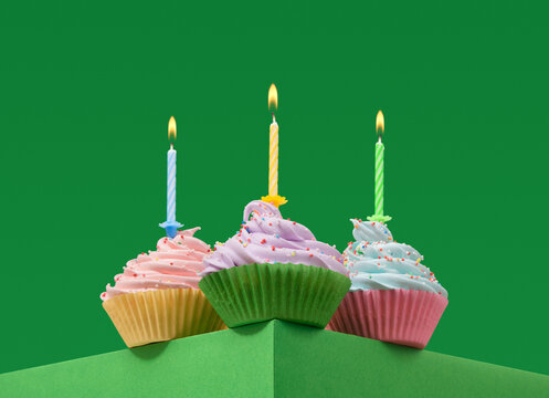 Three festive birthday cupcakes with burning candles on a green background. Concept of birthday party.