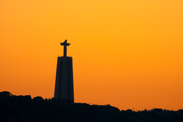 The silhouette of the iconic Christ monument looking over the Tagus River at sunset, Lisbon,...