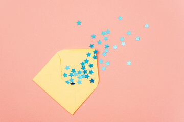 Yellow envelope with blue confetti on pink background. Holiday concept. Top view, flat lay