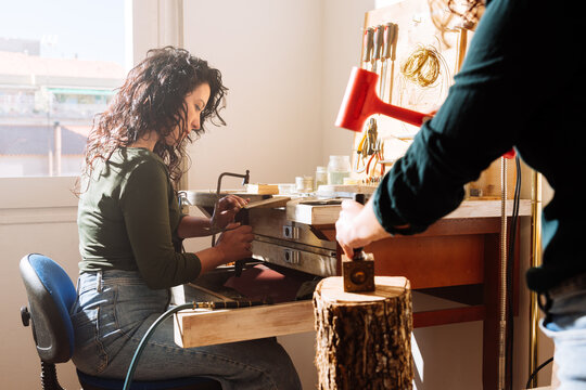 Two skilful female jewellers making accessories in workshop using hammer and hacksaw - Powered by Adobe