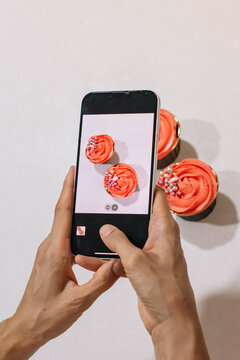 Woman's hand taking a cell phone picture of cupcakes decorated with buttercream and sprinkles
