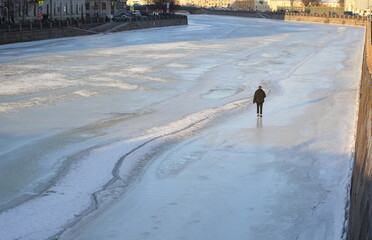 A young man walks on the ice of a frozen river in the city, Fontanka River, St. Petersburg, Russia, January 30, 2024