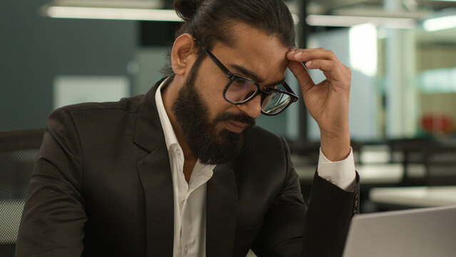 Thoughtful sad worried anxious hard decision problem tired headache Arabian business man thinking online trouble work male pensive manager working on laptop computer in office serious businessman
