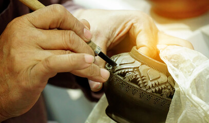 Obraz na płótnie Canvas Craftsman hands carved on clay pottery with traditional pattern by skilled professionals. Photo at local market for community small business, at workplace in rural, thailand.