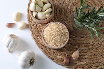 Dehydrated garlic granules in bowl, rosemary and fresh cloves on white table, flat lay