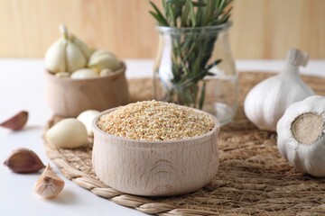 Dehydrated garlic granules in bowl, fresh bulbs and cloves on white table