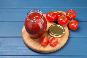 Organic ketchup in jar and fresh tomatoes on blue wooden table. Tomato sauce