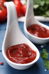 Organic ketchup in spoons on blue wooden table, closeup. Tomato sauce