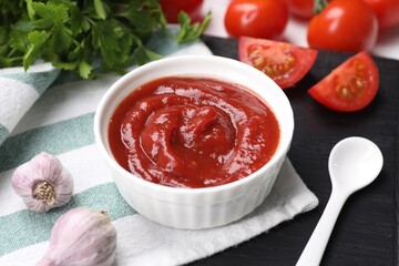 Organic ketchup in bowl, fresh tomatoes and garlic on table, closeup. Tomato sauce