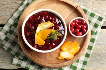 Cranberry sauce in bowl, fresh berries, rosemary and orange peels on wooden table, top view