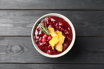 Fresh cranberry sauce, rosemary and orange peel in bowl on black wooden table, top view