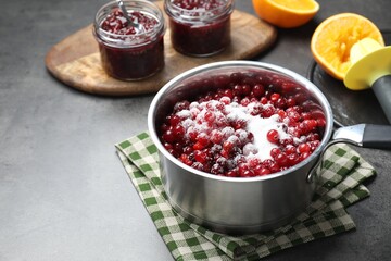 Making cranberry sauce. Fresh cranberries with sugar in saucepan and ingredients on gray table, space for text