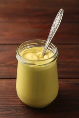 Tasty mustard sauce and spoon in glass jar on wooden table