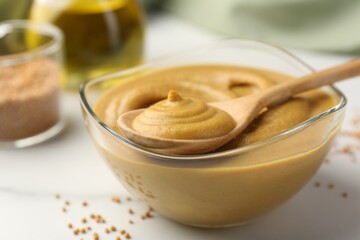 Spoon and glass bowl with tasty mustard sauce on white table, closeup