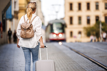 Solo traveler. Woman tourist with backpack pulling suitcase and walking on street. Travel and...