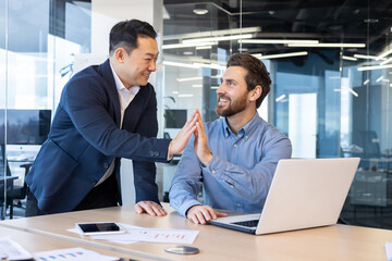 Two businessmen high-fiving in an office, portraying success, teamwork, and partnership in a corporate setting.