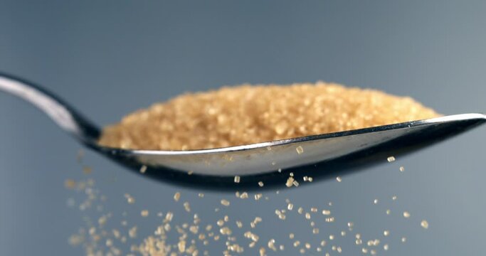 Super slow motion macro of sweet refined granulated brown sugar is falling down with crystal grains from silver spoon isolated on soft background at 1000 fps.