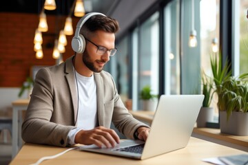 Fototapeta premium A man wearing headphones sits at a desk, focused on his laptop, while engaged in video editing work.