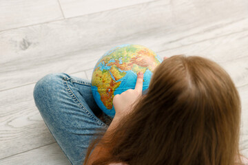 girl sitting on the floor unwinds the globe pointing her finger at India