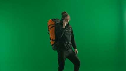 A male traveler with a backpack on his back on a green screen. The man is talking on his smartphone, communicating, sharing impressions