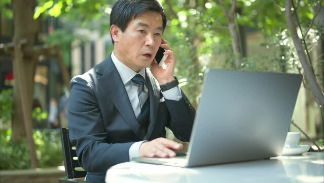 テラス席で電話をする50代男性会社員