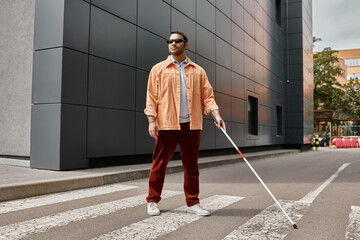 handsome indian blind man in orange jacket with glasses and stick with gray wall on backdrop