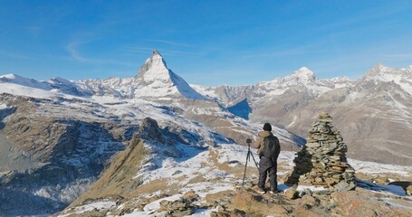 Fototapeta na wymiar Panoramic landscape of Young man backpacker take a photo by camera at Switzerland mountain peak view point with iconic famous landscape Matterhorn background. Nature, Travel and Adventure concept.
