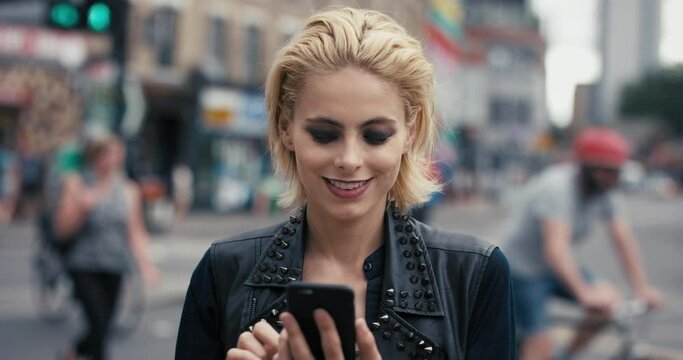 Woman, face and fashion in city with smartphone and happy connection or text with technology. Young person, smile and portrait with cosmetics, cellphone and leather jacket in town with social media