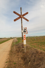 Unterwegs auf einem Schotterweg auf dem Camino Via de la Plata kurz vor Zafra, Extremadura, Spanien. Schilder für den Bahnübergang und gelbe Pfeile als Hinweis für den Pilgerweg