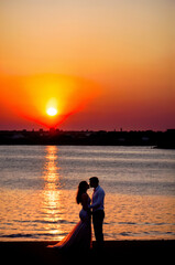Fototapeta premium A man and pregnant woman kiss on a beach as the sun sets. ai generative