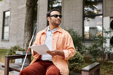 cheerful indian man with visual impairment with glasses sitting on bench and reading braille code