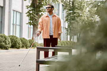 merry indian blind man with glasses and walking stick in vivid orange jacket walking in park