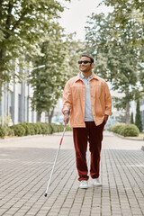 joyful indian blind man with glasses and walking stick in orange vivid jacket walking in park
